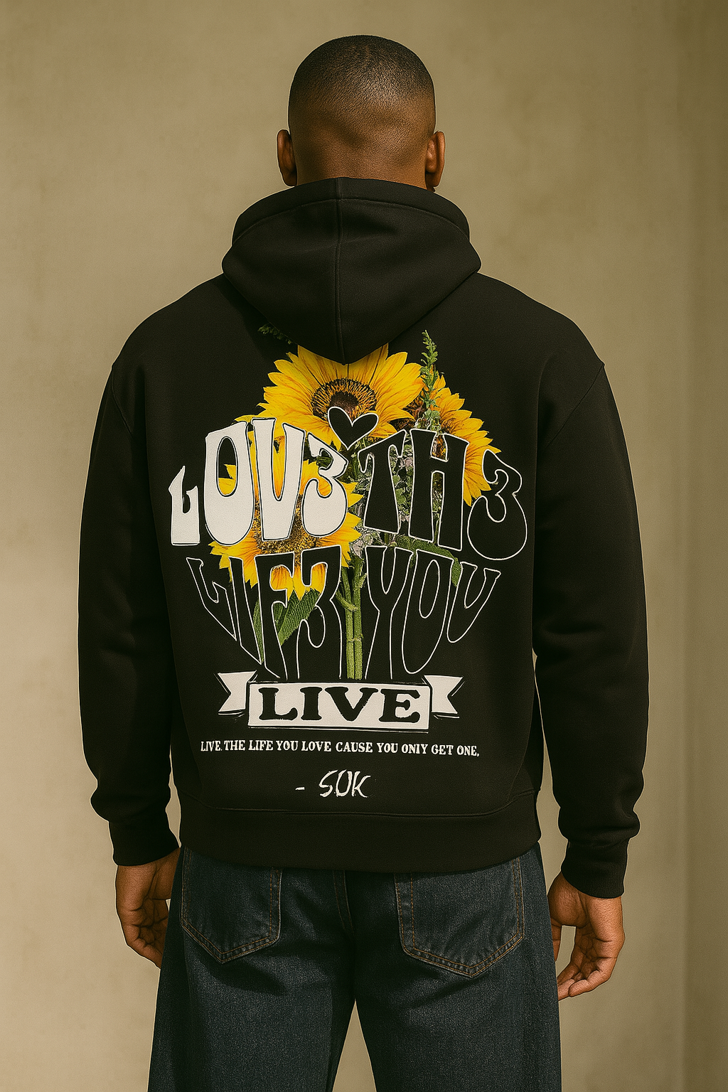 Person wearing a black hoodie with a sunflower design and text on the back against a beige background